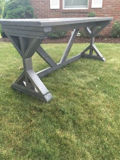 a concrete table sitting in the grass near a house with windows and bushes behind it