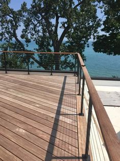 a wooden deck overlooking the ocean with railings and trees in the foreground on a sunny day