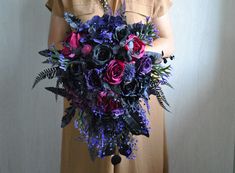 a woman holding a bouquet of purple and red flowers in her hands, with one arm wrapped around the other