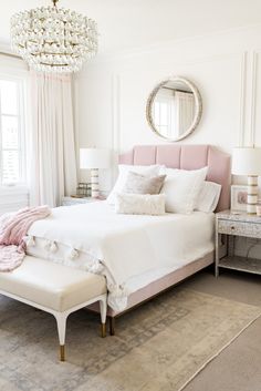 a white bedroom with pink accents and chandelier