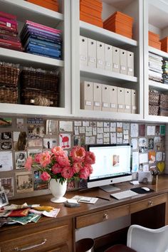 a desk with a computer and flowers on it in front of some bookshelves