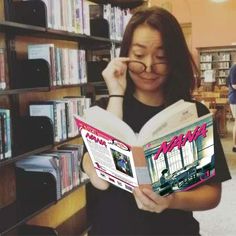 a woman reading a book in front of a bookshelf filled with shelves full of books