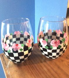 two wine glasses with flowers painted on them sitting on a wooden table next to a mirror