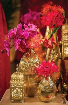 a table topped with vases filled with flowers next to gold containers and candlesticks