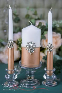 three candles are sitting on a table with flowers in the background