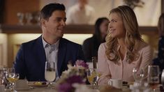 a man and woman sitting at a table talking to each other in front of wine glasses