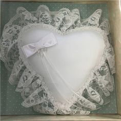 a heart shaped pillow in a box with white lace on the edges and a bow at the top