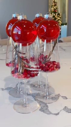 three wine glasses are sitting on a table with red balls and branches in them,