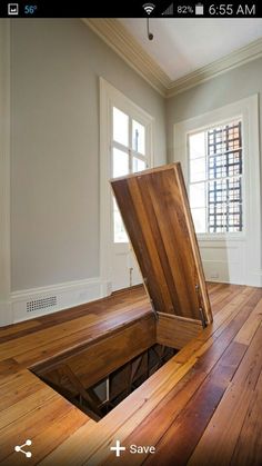 an open wooden box sitting on top of a hard wood floor next to two windows