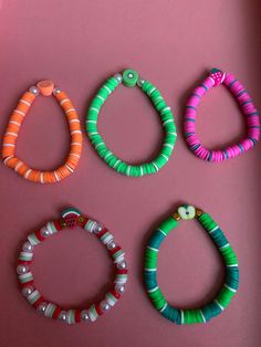 four different bracelets are arranged on a pink surface and one is green, the other is orange