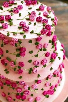 a three layer cake with pink frosting and flowers on the top is sitting on a plate