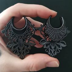 a person holding two black earrings in their hand and one has an intricate design on it