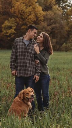 a man and woman are standing in the grass with their dog