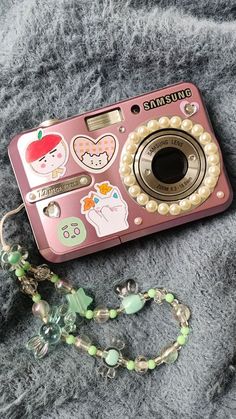 a pink camera sitting on top of a blanket next to a necklace and keychain