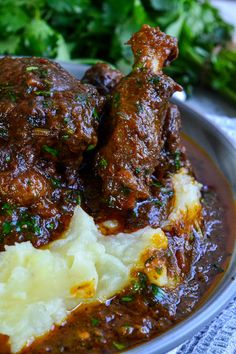 a plate with meat and mashed potatoes covered in gravy, garnished with parsley