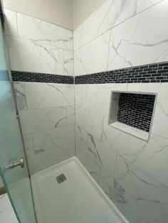 a bathroom with a glass shower door and white marble tiles on the walls, along with a walk in shower