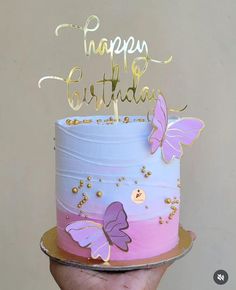 a birthday cake decorated with butterflies and the words happy birthday written on top is being held up by a person's hand