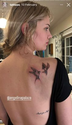 a woman with a bird tattoo on her upper back shoulder and behind her is a mirror