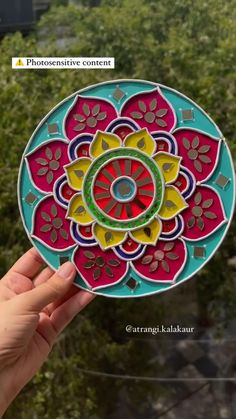 a hand holding up a colorful paper cutout with flowers on the center and bottom