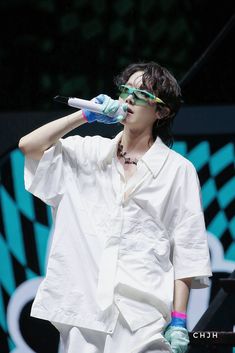 a man in white shirt and blue gloves holding a toothbrush to his mouth while standing on stage