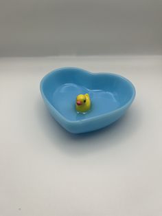 a blue bowl with a yellow rubber ducky in it's center, on a white surface