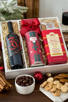 two bottles of wine, crackers and cookies in a box on a wooden table