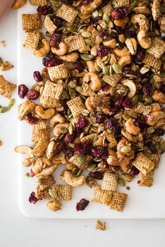 mixed nuts and cranberries on a white cutting board next to an orange napkin