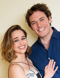 a man standing next to a woman in front of a white wall smiling at the camera