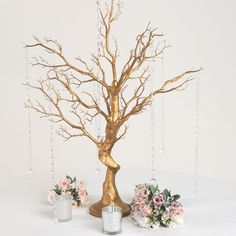 a gold tree with candles and flowers on a white tablecloth next to two vases