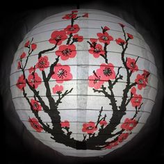 a paper lantern decorated with red flowers and black branches on a white ball in the dark