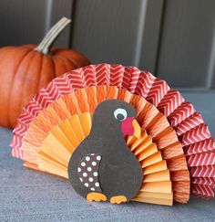 a paper turkey sitting next to a pumpkin