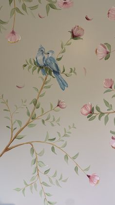 two blue birds sitting on top of a tree branch with pink flowers and green leaves