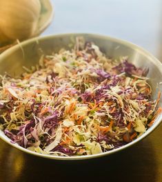 a bowl filled with coleslaw and carrots on top of a wooden table