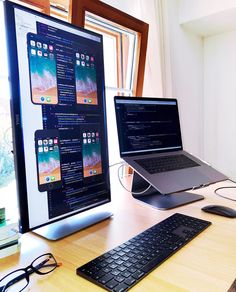 two laptops and a desktop computer on a wooden desk in front of a window