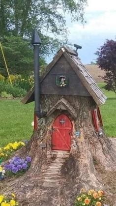 a tree stump with a house built into it and flowers growing around the base in front