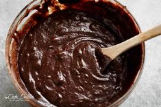 a wooden spoon is in a bowl filled with chocolate cake batter on a gray surface