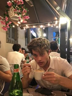 a young man sitting at a table with a cup of coffee in front of him