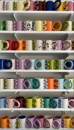 many different colored coffee mugs are on shelves