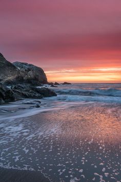 the sun is setting at the beach with waves coming in to shore and pink clouds