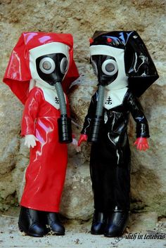 two toy figures wearing gas masks standing next to each other in front of a rock wall