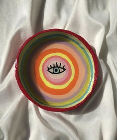 a bowl with an eye painted on it sitting on a white cloth covered tablecloth