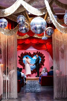 a man and woman standing in front of a stage with balloons hanging from the ceiling