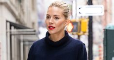 a woman in a blue sweater and red lipstick walking down the street with her hand on her hip