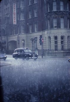 a black and white photo with an old car driving down the street in the rain