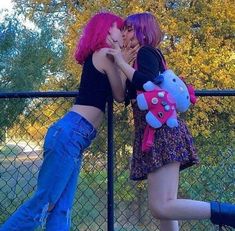 two girls with pink hair are touching each other's noses while standing next to a fence