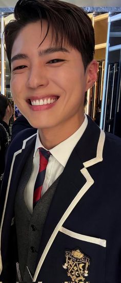 a young man wearing a suit and tie smiling at the camera with other people in the background