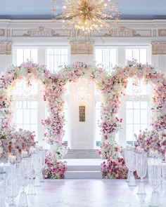 an elegant wedding setup with pink and white flowers on the wall, chandelier and glass vases