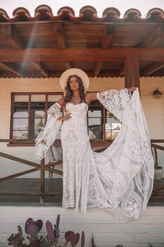 a woman in a white dress and hat standing on a porch with her arms outstretched