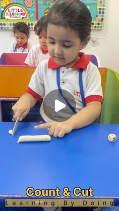 a little boy cutting something with a pair of scissors at a blue table in front of other children