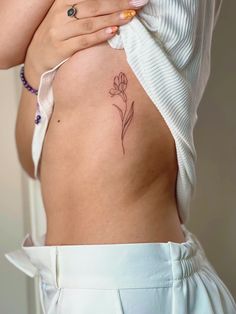 a woman's back with a small flower tattoo on her left side ribcage